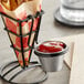 A Clipper Mill wire basket with a sauce cup of ketchup inside holding french fries.