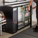 A person opening an Avantco back bar refrigerator filled with beer bottles.