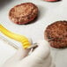 A person using a yellow DuraNeedle probe to cut a hamburger patty.