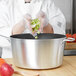 A woman in gloves using a Vollrath Wear-Ever sauce pan to cook vegetables in a school kitchen.