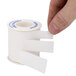 A hand holding a white roll of Medique adhesive tape with blue writing.