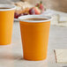 Two Creative Converting Pumpkin Spice Orange paper hot cups filled with coffee on a table.