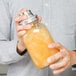 A person using a Tablecraft mason jar cocktail shaker to mix orange liquid.