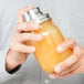 A person holding a Tablecraft Mason Jar Cocktail Shaker filled with orange liquid.