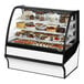 A True refrigerated bakery display case with a variety of cakes, including white frosted cakes with strawberries and berries.