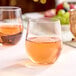 A clear plastic stemless wine glass filled with a light pink beverage.