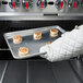 A person holding a Chicago Metallic wire in rim sheet pan of cinnamon rolls.