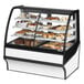 A True dual service refrigerated bakery display case with curved glass on a counter with various baked goods inside.