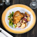 A Kanello white melamine plate with a yellow edge holding chicken, potatoes, and asparagus on a table.