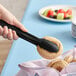 A hand holding a pastry with a black Cambro scallop grip tong.