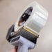 A person's hand holding a roll of Shurtape general purpose fiberglass reinforced strapping tape.