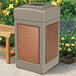 A beige StoneTec square trash can with Sedona panels next to a wooden bench.