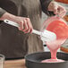 A person using a white Rubbermaid spatula to mix pink liquid in a glass bowl.