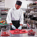 A chef cutting meat on a Rubbermaid red cutting board.