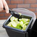 A hand using a spoon to scoop lime wedges into a San Jamar Mini Dome condiment container on a counter.