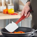 A hand using a Rubbermaid red high temperature silicone spatula to stir food in a pan.