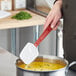 A person using a Rubbermaid red silicone spoonula to stir a pot of soup.