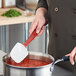 A person using a Rubbermaid red silicone spoonula to stir a pot of red sauce.