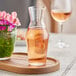 A Reserve by Libbey glass carafe filled with liquid on a wooden tray with a glass of liquid and a vase of flowers.