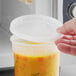 A hand using a ChoiceHD translucent plastic deli container lid on a container of soup.