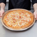 A man holding a pizza on a Solut Kraft Eco Natural pizza tray.