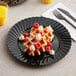 A WNA Comet black plastic plate with waffles, raspberries, and whipped cream on it.