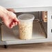 A hand reaching out to a ChoiceHD translucent plastic deli container of food in a microwave.