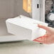 A person's hand holding a white Choice microwavable take-out box.