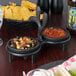 A black metal dish with two black bowls of salsa and a bowl of chips on a table.