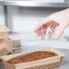 A hand holding a Solut clear plastic lid over a loaf of bread.