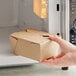 A hand holding a Choice Kraft folded paper take-out box in front of a microwave.