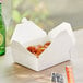 A white folded paper take-out container filled with food on a table.