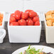 A Tablecraft white bowl filled with cherry tomatoes on a table of food.