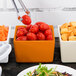 A Tablecraft orange bowl of tomatoes on a table in a salad bar.