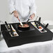 A chef using a Tablecraft black brushed aluminum induction station kit on a black rectangular table.