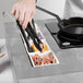 A chef using tongs to prepare food in a pan using the Tablecraft Random Swirl Aluminum Double Countertop Induction Station.