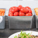 A Tablecraft Contemporary Collection natural and pewter bowl filled with tomatoes on a salad bar counter.