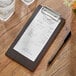 A Choice dark wood menu holder with a receipt on it sitting on a table.