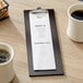 A dark wood Choice menu holder with a menu on a table with coffee cups and a basket of cookies.