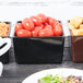 A black Tablecraft bowl in a salad bar filled with tomatoes.