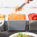 A person using a knife to cut a carrot into a gray Tablecraft straight sided bowl.