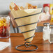 A black iron Clipper Mill spiral wire cone basket holding fries on a table.