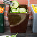 A person using a knife to cut cucumbers on a table near a maroon speckled bowl.