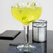 A Libbey Super Margarita Glass filled with a yellow drink and lime slices.