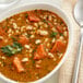 A bowl of soup with vegetables and herbs including dried small white beans.