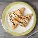 A Kanello ivory melamine plate with a Kanello green rim holding two pastries drizzled with chocolate sauce.