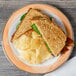 A Kanello Diamond White melamine plate with a sandwich, potato chips, and bacon on a wood table.