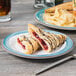 A Kanello white melamine plate with a sandwich and pastries on it.