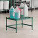 A Regency green epoxy dunnage shelf holding white containers and jugs.