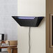 A black rectangular Lavex Zap N Trap wall sconce with a wire attached to a white wall.